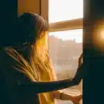 Femme au soleil devant une fenêtre, lumière du matin
