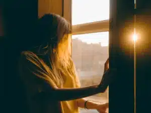 Femme au soleil devant une fenêtre, lumière du matin