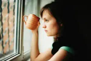 Femme fatiguée à la fenêtre avec une tasse, le matin : la fatigue persistante ne vient pas toujours d un manque de vitamines