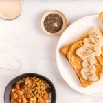 Vue de dessus d'un repas avec tartine au beurre de cacahuète et banane, avoine, noix et lait — illustration des apports en protéines et calories.