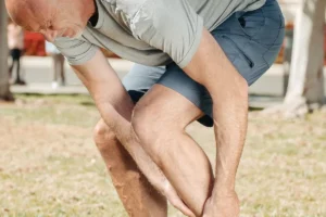 Coureur penché tenant son mollet et sa cheville dans un parc, article sur les blessures du coureur et la nutrition au Maroc