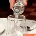 Une table dressee avec des assiettes servies et une main qui verse de l eau dans un verre