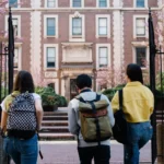 ثلاثة طلبة بحقائب ظهر مصوَّرون من الخلف أمام بوابة جامعة، مقال الجري للشباب في المغرب