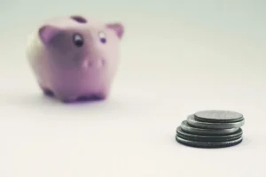 حصالة وردية غير واضحة في الخلفية وقطع نقدية مكدّسة في المقدمة، مقال ميزانية مكمّلات العداء في المغرب