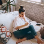 Femme assise près d'une fenêtre écrivant dans un carnet, photographie d'illustration