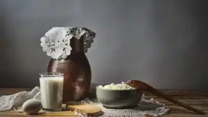 Photographie d’illustration : verre de lait, fromage frais dans un bol, pichet en terre et œuf sur une table en bois