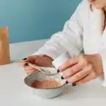 Une femme melange une poudre dans un verre d eau dans une cuisine, lumiere du matin
