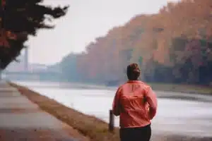 Coureuse vue de dos en veste orange sur un chemin au bord de l'eau, guide running et nutrition pour les femmes au Maroc