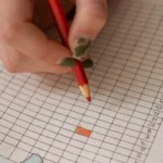 Main notant le suivi des symptômes sur une grille de carnet, photographie d'illustration