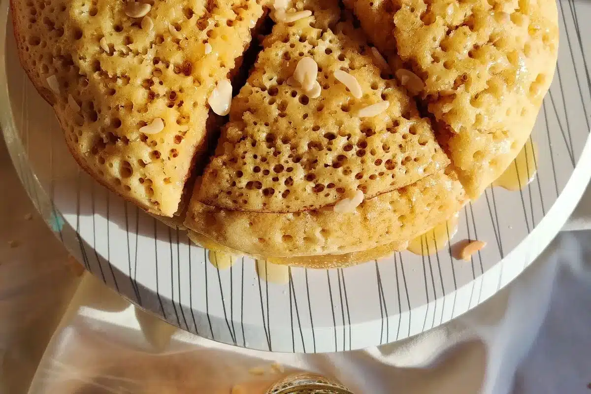 Baghrir marocain au miel et aux amandes sur une table ensoleillée, guide de ce qu'on mange avant de courir au Maroc