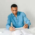 Un adulte révise avec un livre et des feuilles sur son bureau, photographie d’illustration.