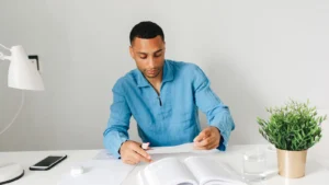 Un adulte révise avec un livre et des feuilles sur son bureau, photographie d’illustration.