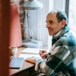 راجل جالس فمكتب فالدار، قدّامو حاسوب ودفتر، صورة فوتوغرافية توضيحية.