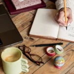 يد كاتكتب فدفتر للتنظيم حدا حاسوب، صورة فوتوغرافية توضيحية.