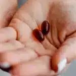 Une main ouverte tenant deux capsules de complement alimentaire, lumiere naturelle