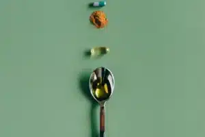 Une gélule, une poudre, une capsule d'huile et une cuillère alignées sur un fond vert, guide honnête des suppléments pour coureurs au Maroc