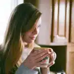 Une femme tient une tasse chaude pres d une fenetre, lumiere d hiver