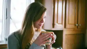 Une femme tient une tasse chaude pres d une fenetre, lumiere d hiver