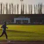 Un homme court sur une piste d athletisme au lever du soleil, stade en arriere plan