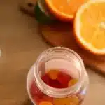 Un bocal de complements ouvert sur une planche en bois avec des agrumes coupes, dans une cuisine