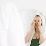 شابة كتدير روتين العناية بالوجه قدام المراية، صورة توضيحية