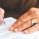 يدين كيوقّعو على ورقة فوق مكتب خشبي